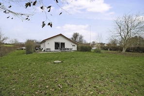Una casa a un piano con un portico, un piccolo prato e un albero sullo sfondo.