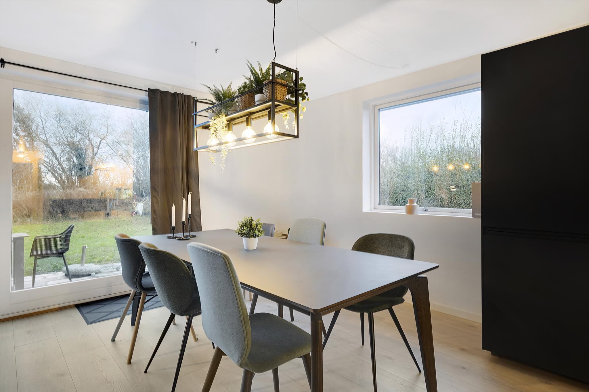 Comedor con mesa, sillas, una lámpara colgante y vistas amplias a través de grandes ventanales.