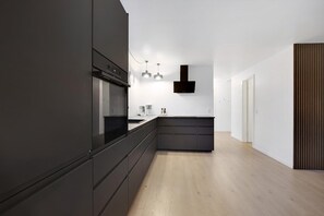 A modern kitchen with dark cabinetry, a built-in oven, and pendant lighting. - Beautiful newly renovated summer house by the sea (Frørup)