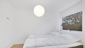 Ett sovrum med en säng, ett fönster med utsikt och en hängande lampa.