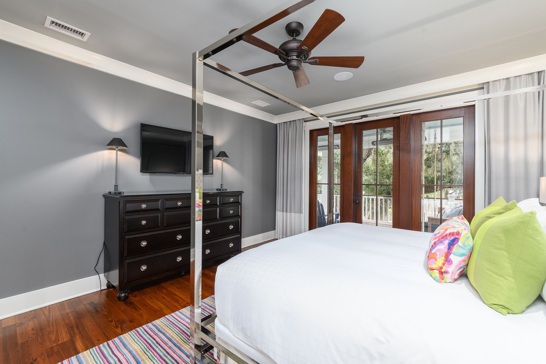 A bedroom with a bed, a ceiling fan, a TV, a dresser, and a window with curtains.