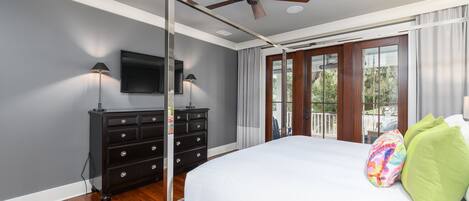 A bedroom with a bed, a ceiling fan, a TV, a dresser, and a window with curtains.