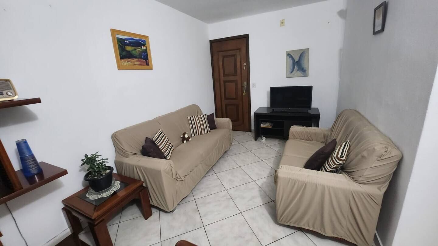 Een woonkamer met twee beige banken, een kleine houten tafel met een plant, een tv-meubel en een deur.