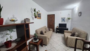 Ein Wohnzimmer mit zwei beigefarbenen Sofas, einem Holztisch, einem Fernsehschrank, einer Uhr und verschiedenen Topfpflanzen.