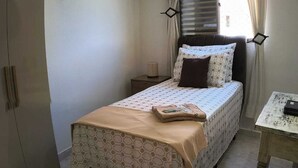 Ein kleines Schlafzimmer mit Bett, Nachttisch, Lampe und einem Fenster mit Vorhängen.