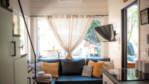Una habitación acogedora con un sofá azul oscuro, cojines amarillos y un ventanal con cortinas de encaje.