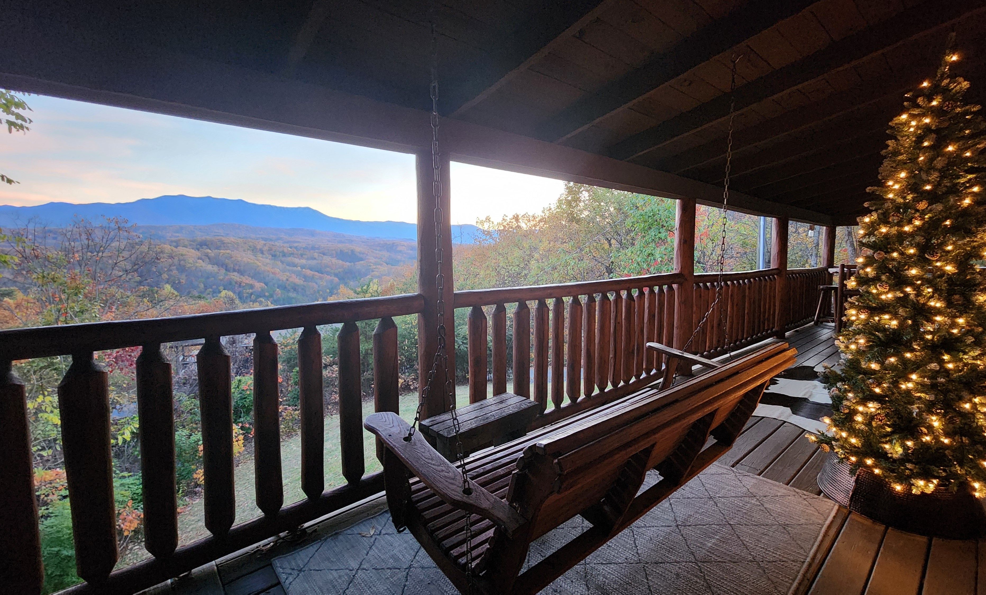 A wooden deck with a bench and a Christmas tree, overlooking a mountainous landscape.