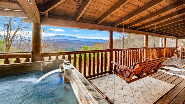 Una terraza de madera con un jacuzzi, bancos de madera y vistas a las montañas.