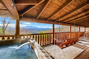 Eine Holzterrasse mit Whirlpool, Holzliegen und Blick auf die Berge.
