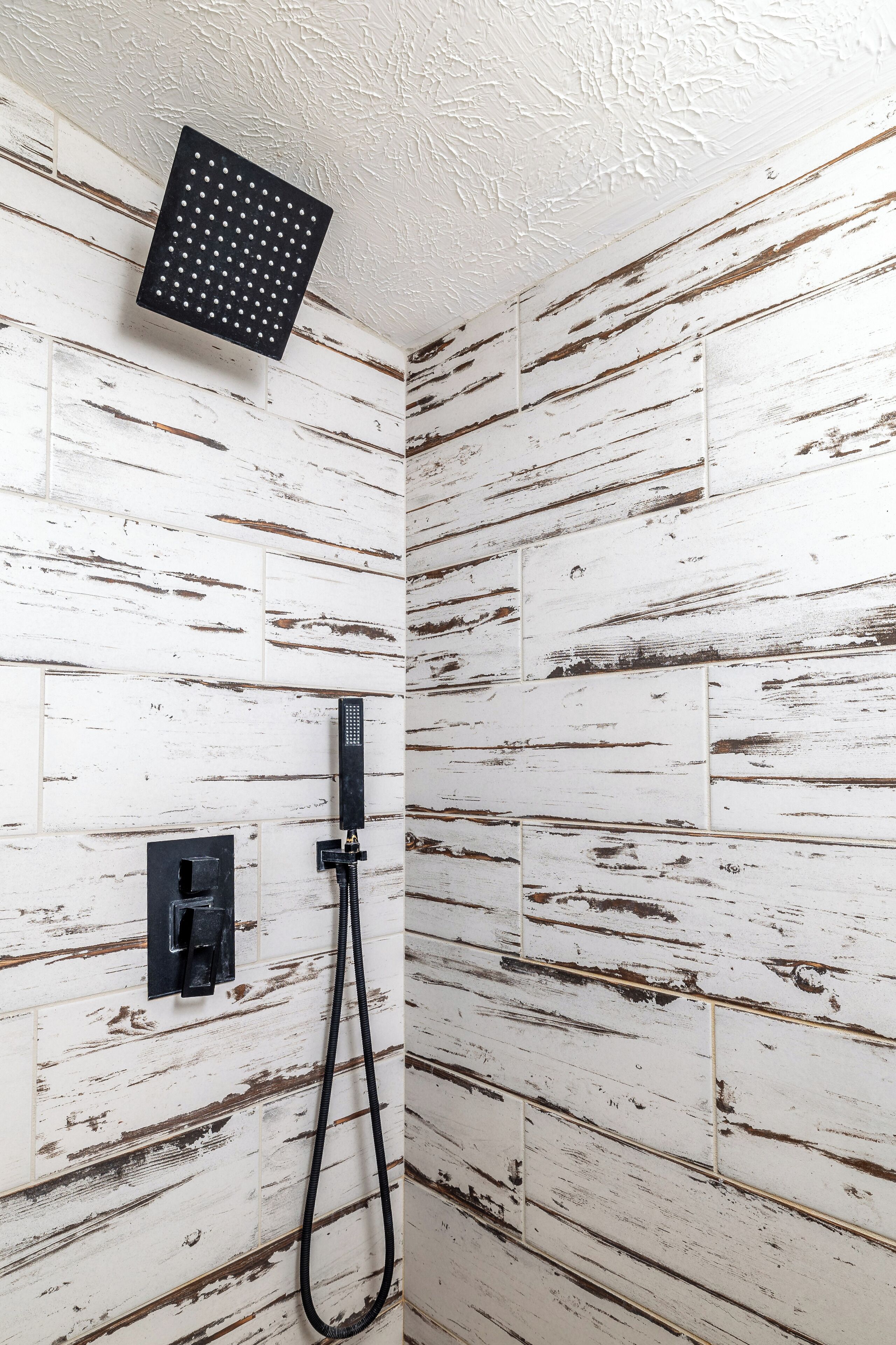 A shower area with a black handheld showerhead and a black hose. The walls are covered with white wooden panels.