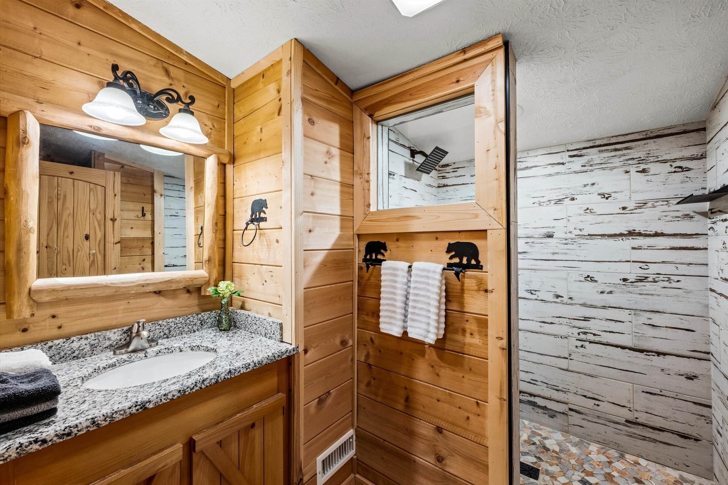 Une salle de bain en bois avec un lavabo en granit, un miroir, un porte-serviettes et un espace douche.