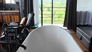 A room with a large bathtub, a chair, a television, and a view of a green landscape through a window. - Sitting on stilts, Stuido Wow has spectacular volcano, lake & rain forest views! (El Castillo)