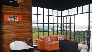 A room with a large window, a bathtub, an orange sofa, and a black chair. - Sitting on stilts, Stuido Wow has spectacular volcano, lake & rain forest views! (El Castillo)