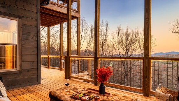 A wooden deck with a view of trees and mountains, a glass door, and a table with a vase and fruit. - New to VRBO!  Theater Seating, Pool Table, Gaming Station, Bunk Rm, Hot Tub (Gatlinburg)