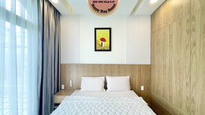 A hotel room with a large bed, a headboard, a framed picture on the wall, and a sign above the bed. - Happy Stay Resort (Ho Chi Minh City)
