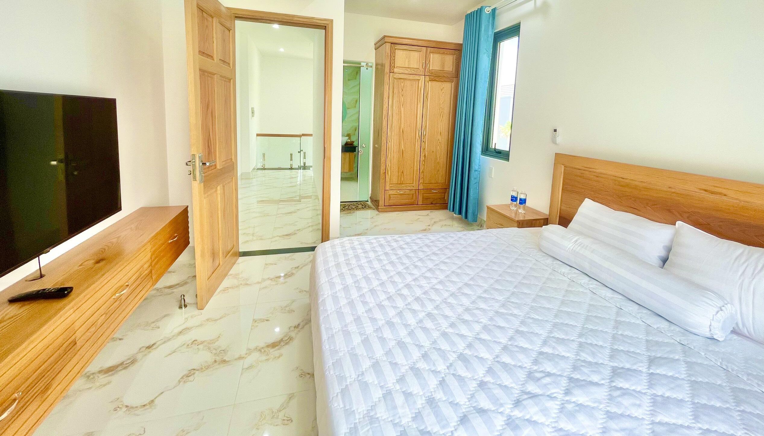 Une chambre d’hôtel avec un lit, une télévision, une armoire en bois et une salle de bain visible à travers une porte ouverte.