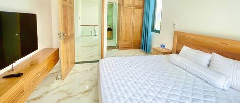 Une chambre d’hôtel avec un lit, une télévision, une armoire en bois et une salle de bain visible à travers une porte ouverte.