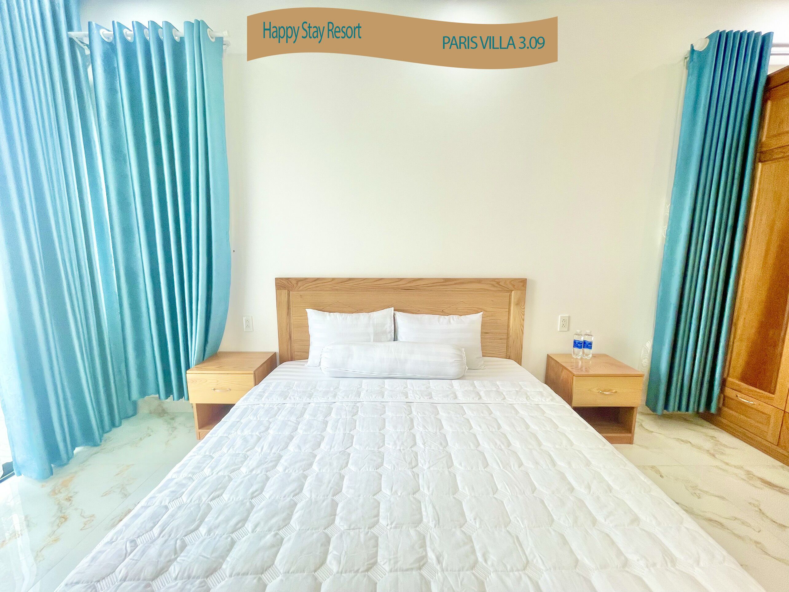 Una habitación de hotel con una cama grande, cabecero de madera, dos mesitas de noche y cortinas azules.
