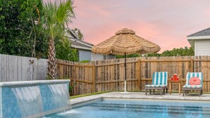 A backyard with a swimming pool, a wooden fence, two striped lounge chairs, and a thatched umbrella. - Sunset Haven by the Pool (Panama City Beach)
