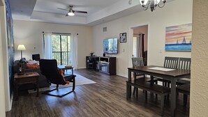 Un salon spacieux comprenant un coin repas, un ventilateur de plafond, un téléviseur et un tableau accroché au mur.