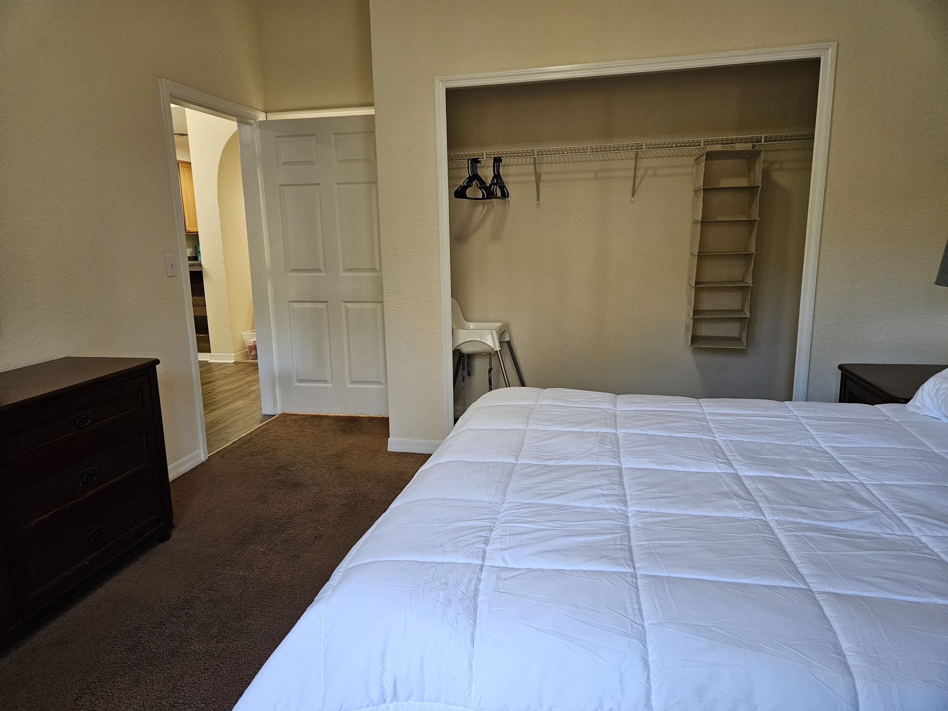 A bedroom with a large bed, a wardrobe, and a door leading to another room.
