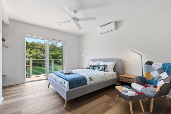 A bedroom with a bed, a chair, a nightstand, a ceiling fan, and a sliding glass door to a balcony.