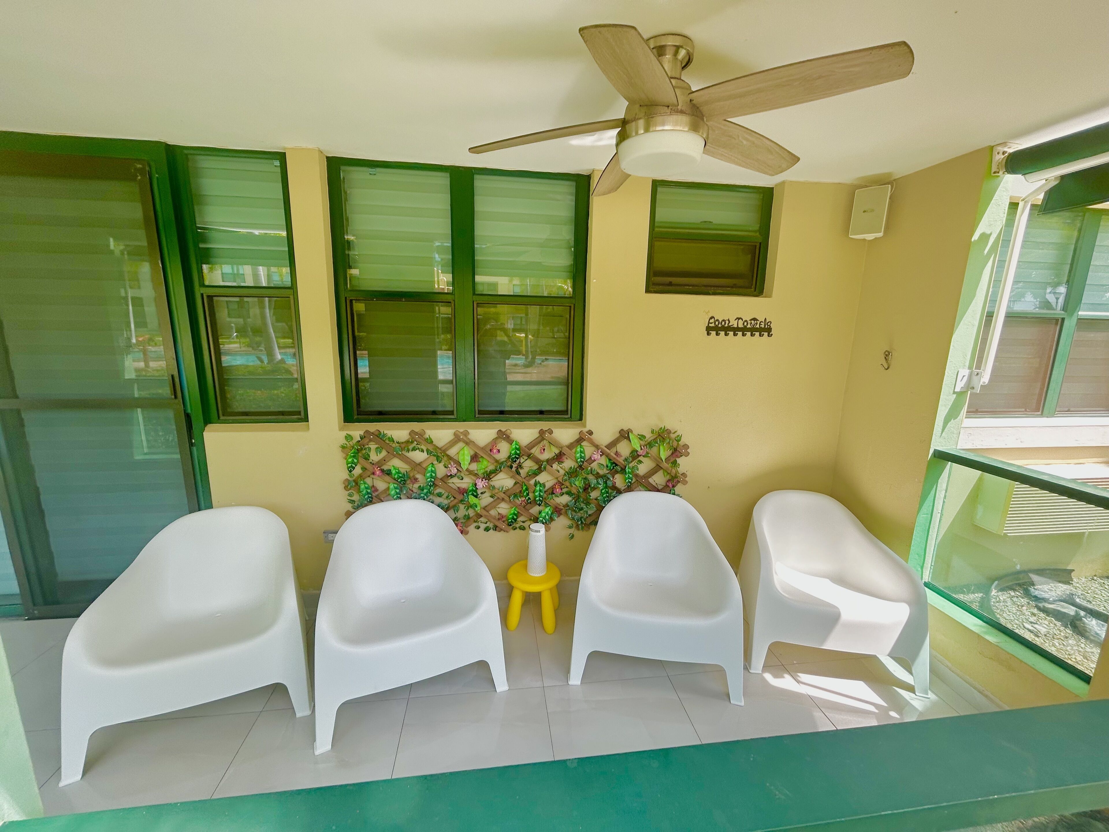 A room with three white plastic chairs, a ceiling fan, and a small yellow stool.