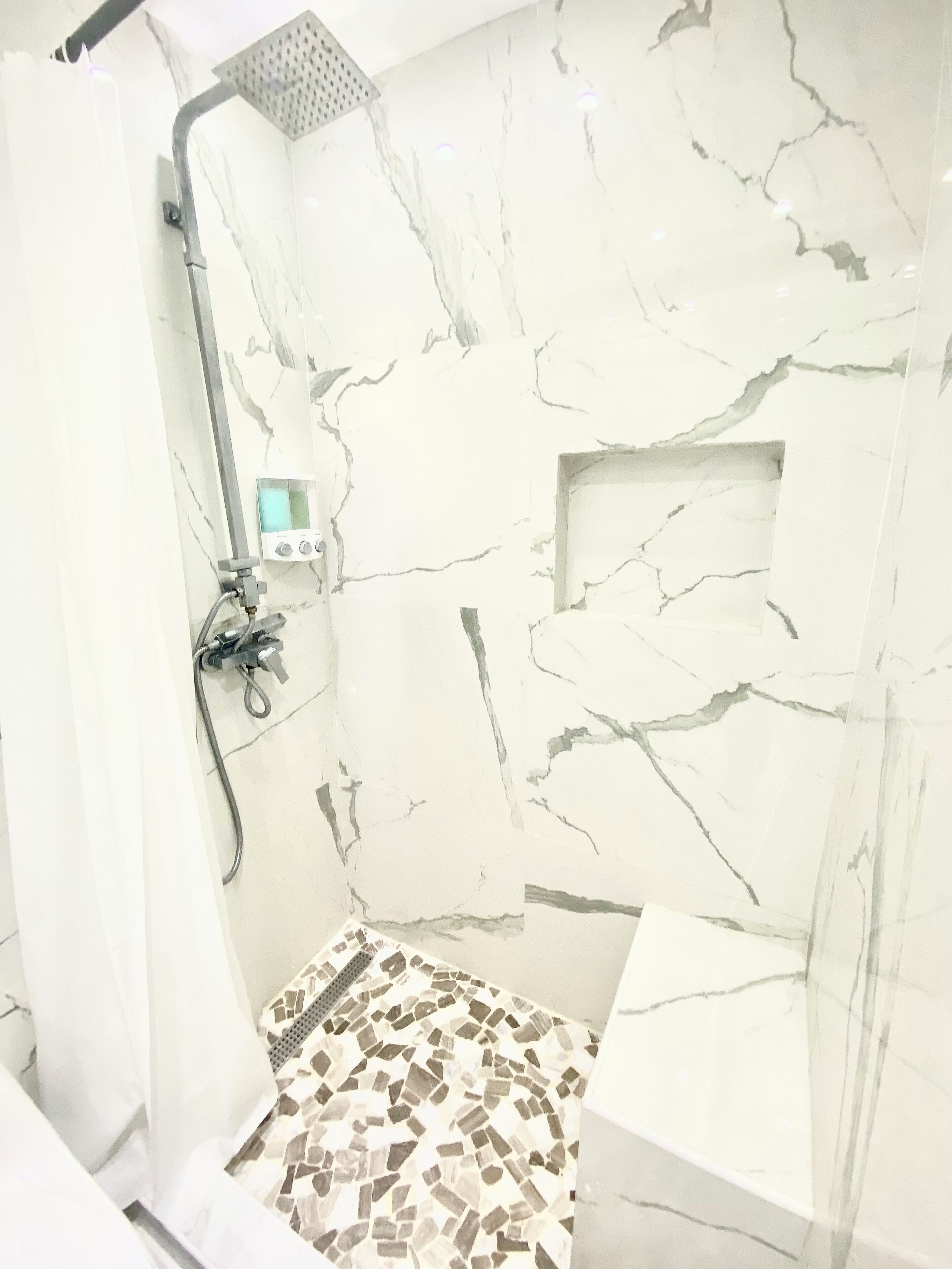 Une douche équipée d’un panneau de commande, d’un pommeau de douche à main et d’un sol carrelé.