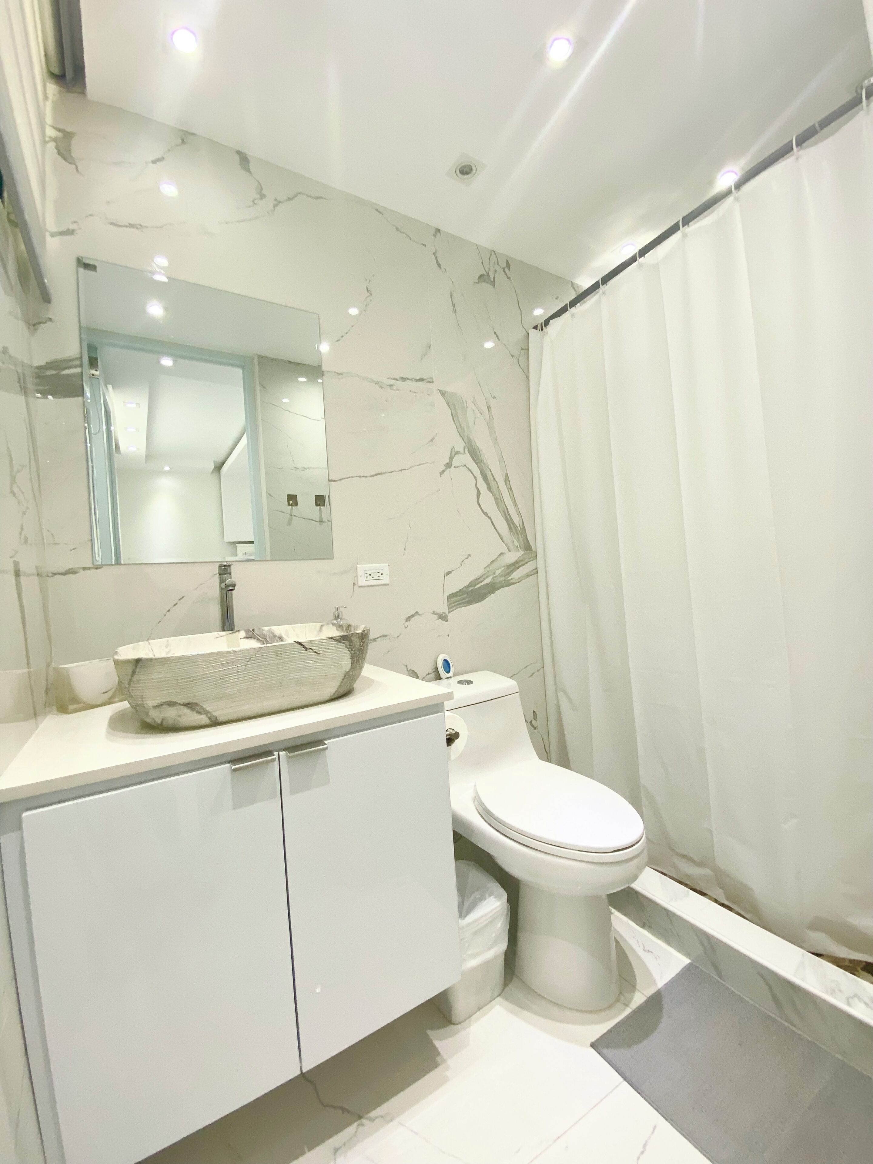 A modern bathroom with a marble sink, a toilet, and a shower curtain.