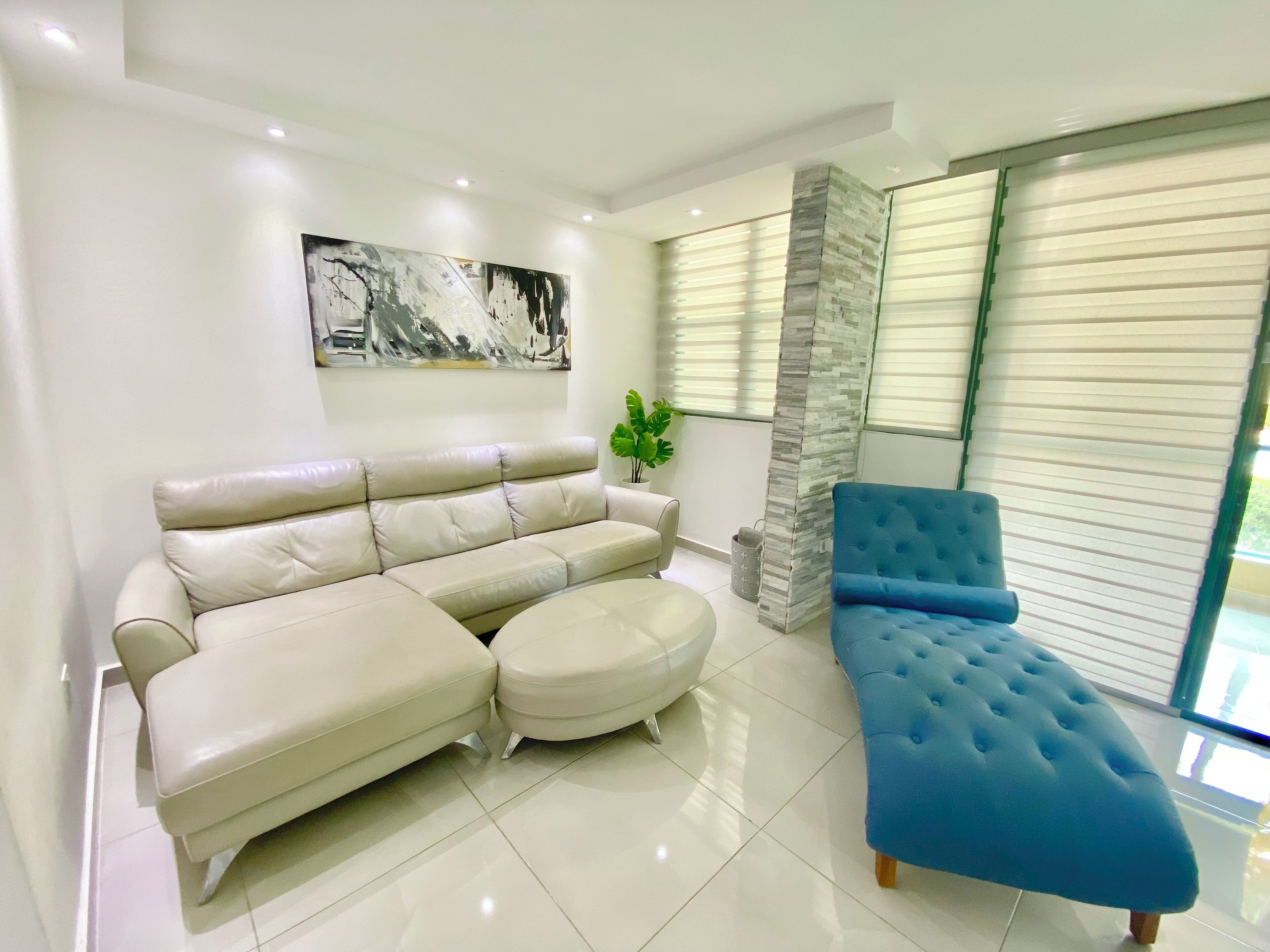 Una sala moderna con un sofá seccional color beige, un otoman azul y una pared de acento de piedra.
