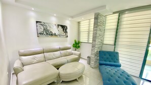 Ein modernes Wohnzimmer mit einem beigefarbenen Ecksofa, einem blauen Pouf und einer Wand aus Stein.