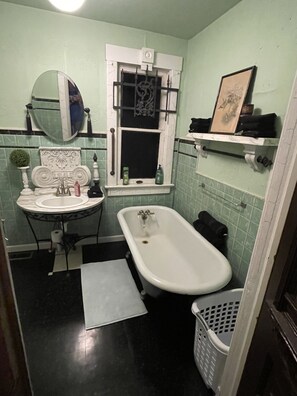 Un baño con lavamanos, espejo, bañera y una pequeña ventana con cortina.