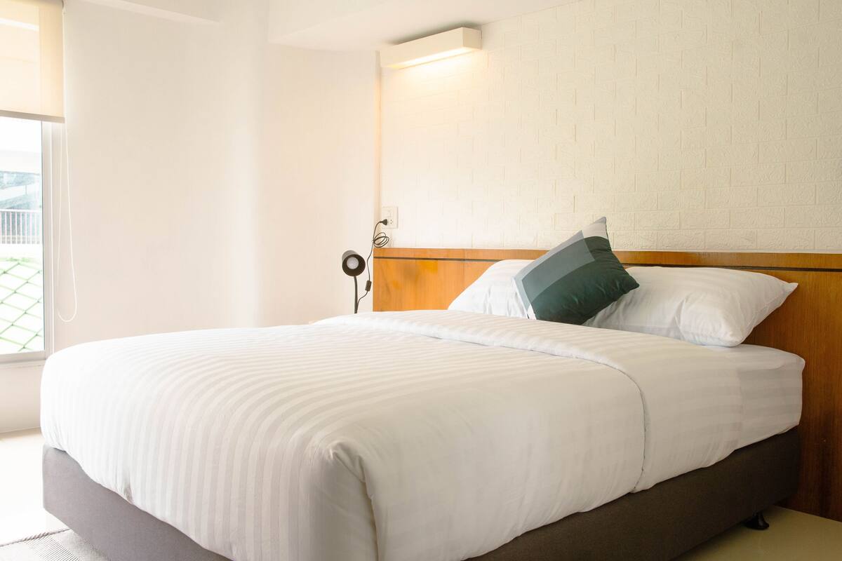 A neatly made bed with a wooden headboard, white bedding, and a single green pillow.