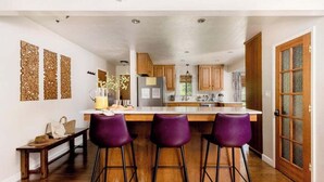 A kitchen with wooden cabinets, a central island with bar stools, and a bench.