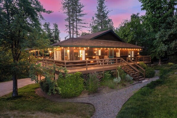 Eine Holzhütte mit einer Terrasse, umgeben von Bäumen und einem Kiesweg.