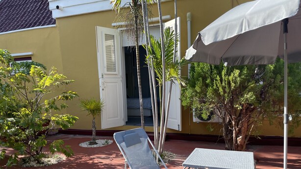 A patio with a table and chairs, a white umbrella, and a door leading to a room.