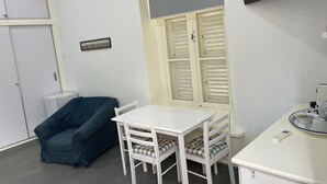 A small, clean room with a white table and chairs, a window with shutters, a blue sofa, and a white cabinet.