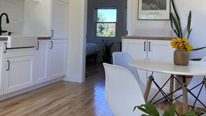A modern kitchen with white cabinets, a wooden ceiling, and a ceiling fan. There is a dining area with a white table and chairs, and a potted plant on the table. - Old Town Oasis - the perfect 30 day stay (Fort Collins)