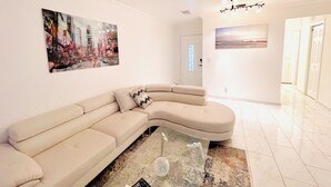 Una sala moderna con un sofá seccional color beige, una mesa de centro de vidrio y un ventilador de techo.