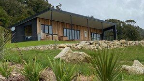 A modern house with a large deck, surrounded by a stone wall and lush greenery.