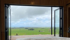 A bedroom with a large window, a bed with a floral bedspread, and a view of a green landscape.