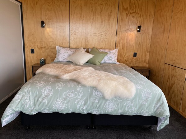 Un lit recouvert d’une couvre-lit à motifs floraux, agrémenté d’un plaid blanc moelleux et de plusieurs coussins, dont un de couleur verte.