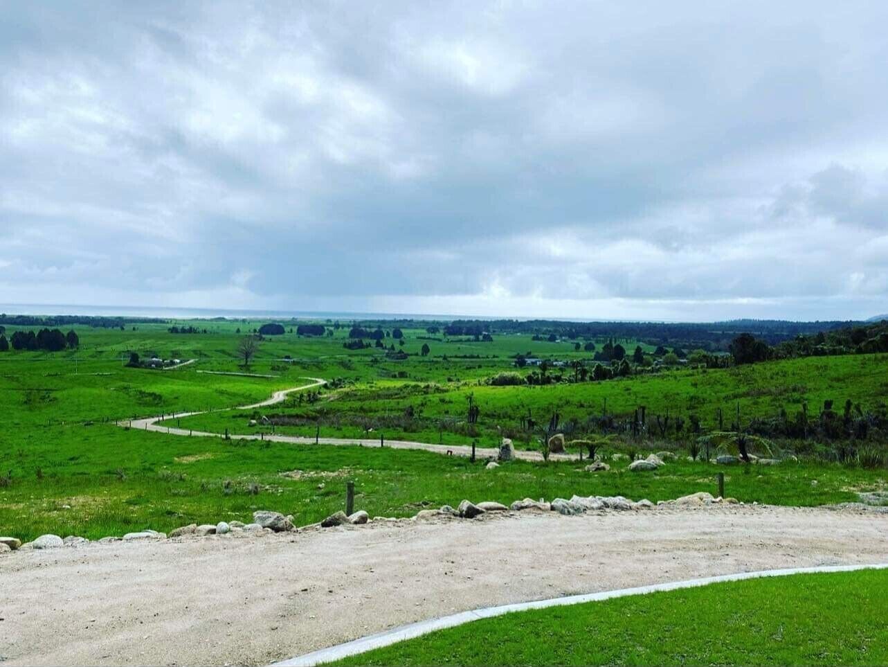 Un paysage rural avec un chemin de terre, des champs verdoyants et un ciel nuageux.