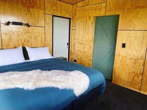 Une chambre avec un grand lit, des murs en bois, une porte verte et un plaid blanc et moelleux.