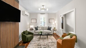 En moderne stue med en sofa, en grøn lænestol og en orange lænestol, et sofabord og et stort vindue med gardiner.