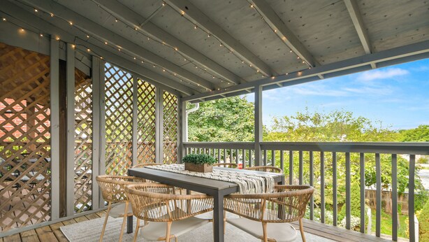 En overdækket terrasse med borde og stole, en tr æterrasse og udsigt til grønne områder.