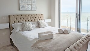 A bedroom with a large bed, a view of the sea through a sliding glass door, and a decorative wall piece above the bed. - West Lodge, Bognor Regis -  a flat that sleeps 4 guests  in 2 bedrooms (Bognor Regis)