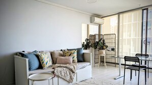 Una sala de estar moderna con un sofá blanco, cojines estampados, una mesa de comedor de vidrio y un atril para planta.
