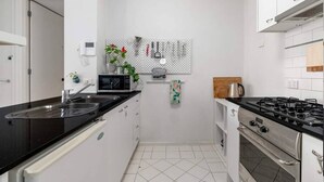 Cocina compacta con armarios blancos, encimera negra, microondas, estufa y un panel de tacos con utensilios de cocina.