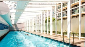 Una piscina interior con paredes de vidrio transparente, una persona nadando y un diseño arquitectónico moderno.